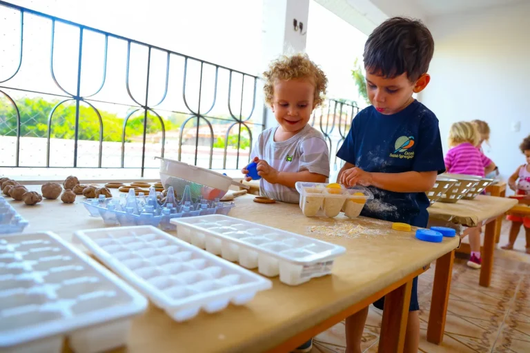 Crianças exploram massa e diferentes recipientes em uma mesa da Escola Sabiá-Laranjeira.