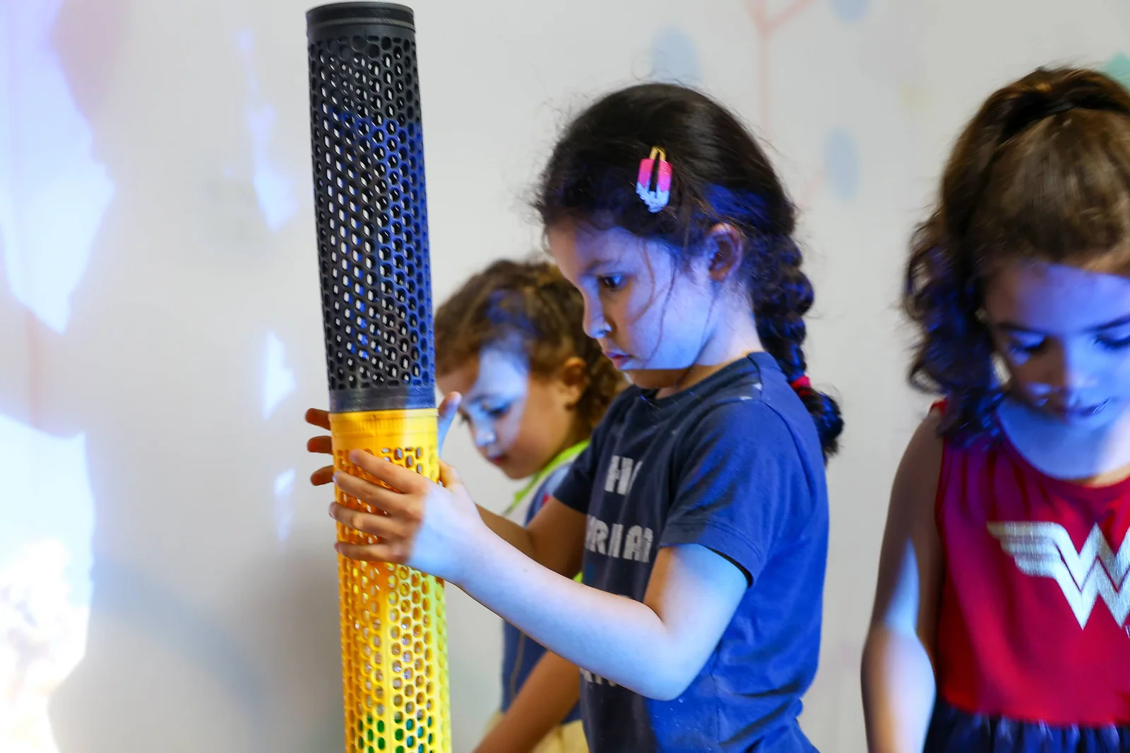 Crianças exploram uma construção com materiais coloridos e projeções de luz.